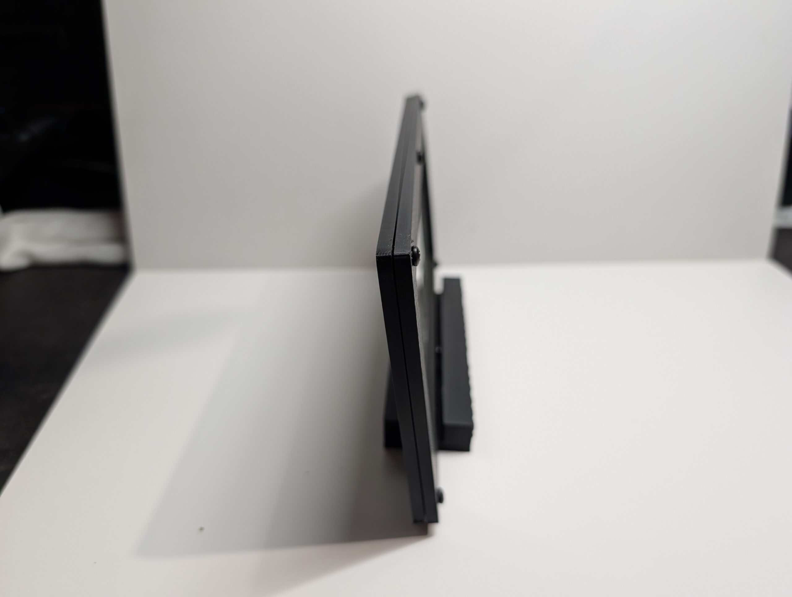 Side view of black carbon fiber Serial Shield 3D currency frame with stand showing thickness